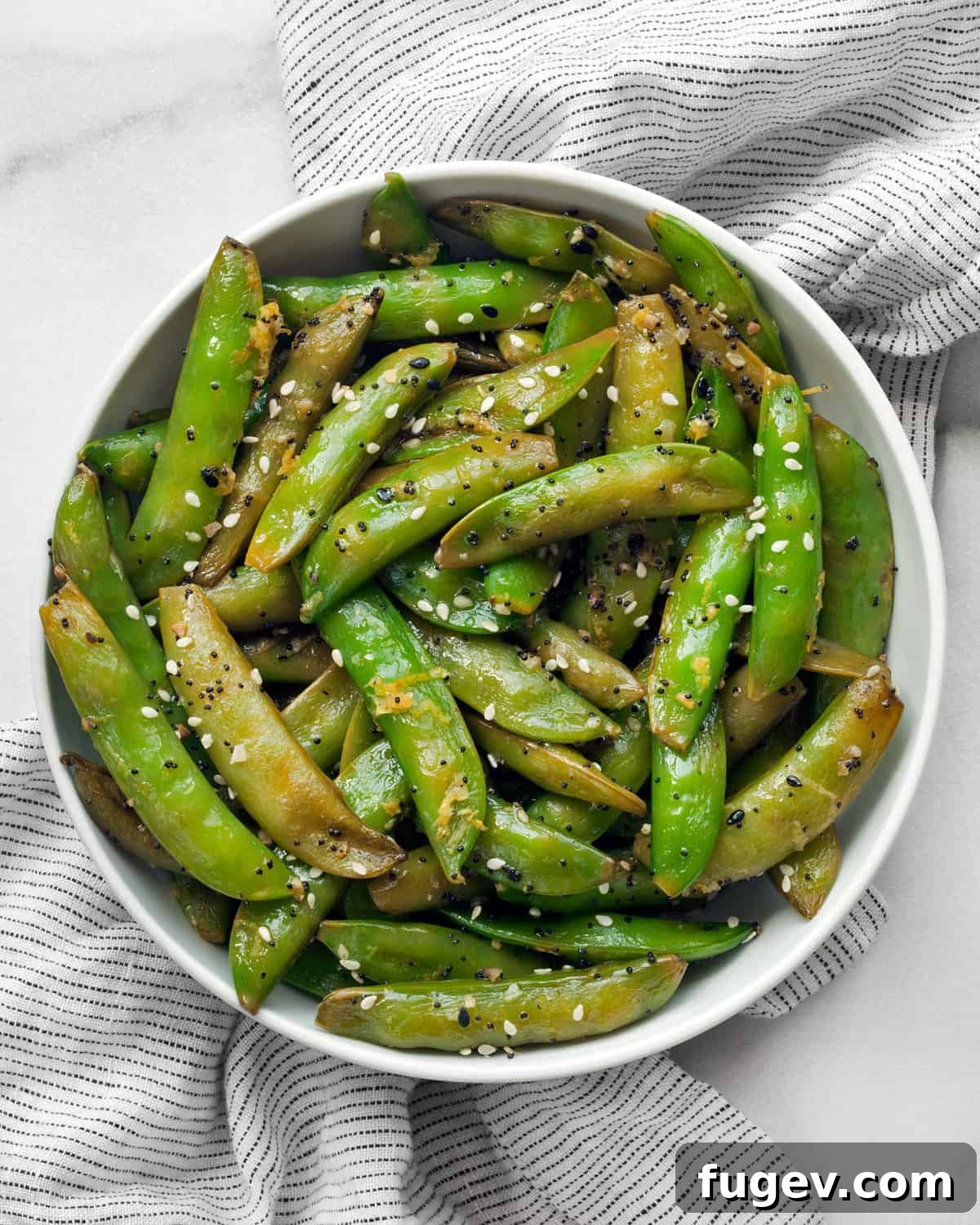 Crisp Garlic Snap Peas 2 A close-up shot of perfectly sautéed sugar snap peas with lemon zest and everything seasoning in a rustic white bowl, ready to be served.