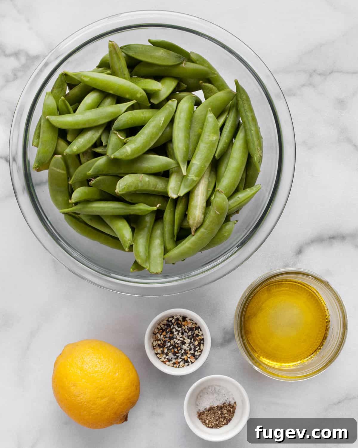 Crisp Garlic Snap Peas 3 All six ingredients for sautéed snap peas laid out: fresh sugar snap peas, a whole lemon, a bottle of olive oil, salt, pepper, and a jar of everything seasoning.