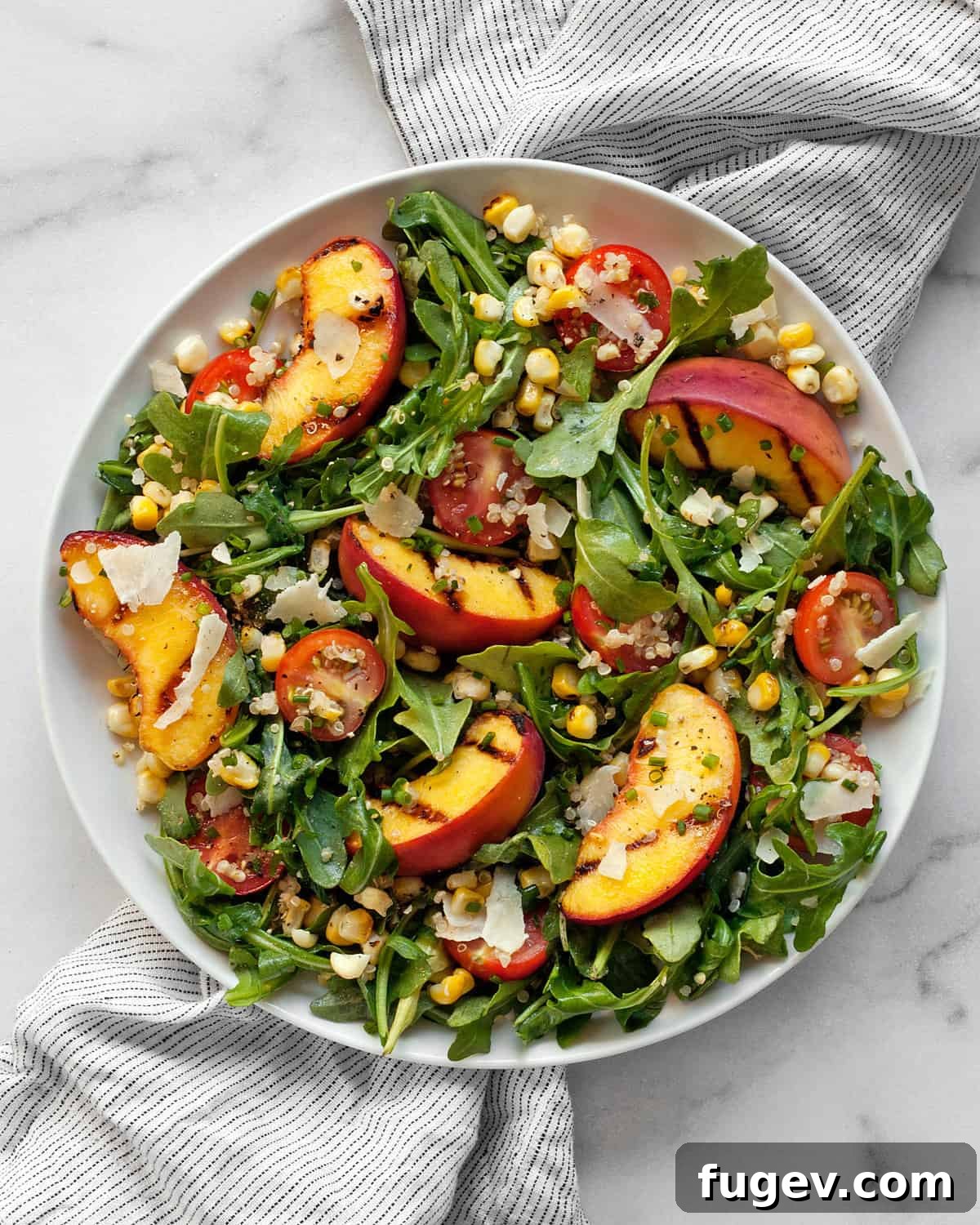 Sweet & Smoky Grilled Peach and Corn Salad 2 Grilled peach salad with corn on a plate, featuring golden peaches, charred corn kernels, green arugula, and red tomatoes.