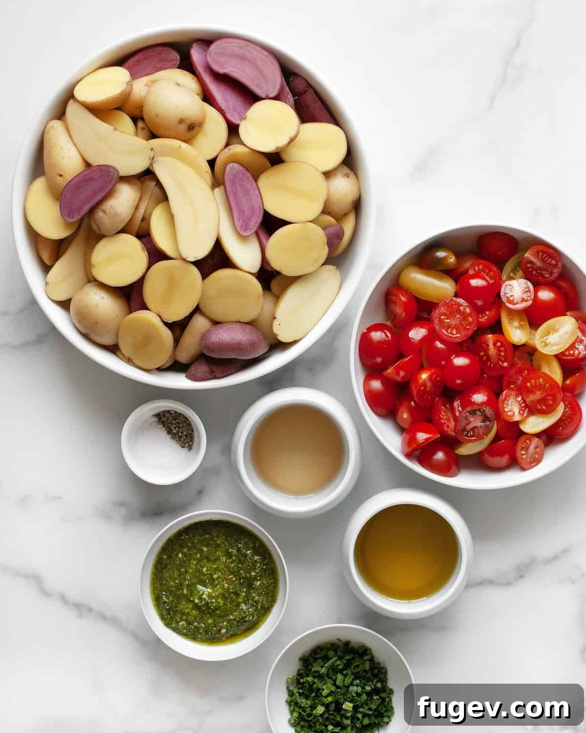 Mediterranean Roasted Tomato Pesto Potato Salad 3 A flat lay of fresh ingredients for pesto potato salad: a bowl of fingerling potatoes, cherry tomatoes, a jar of basil pesto, white wine vinegar, fresh chives, a bottle of olive oil, and small dishes of salt and pepper.