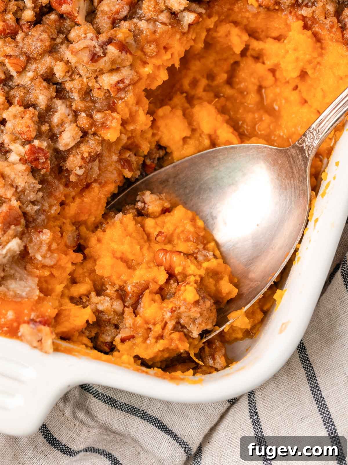 Golden Pecan Sweet Potato Bake 2 A golden-brown sweet potato casserole in a white baking dish, ready to be served with a silver spoon.