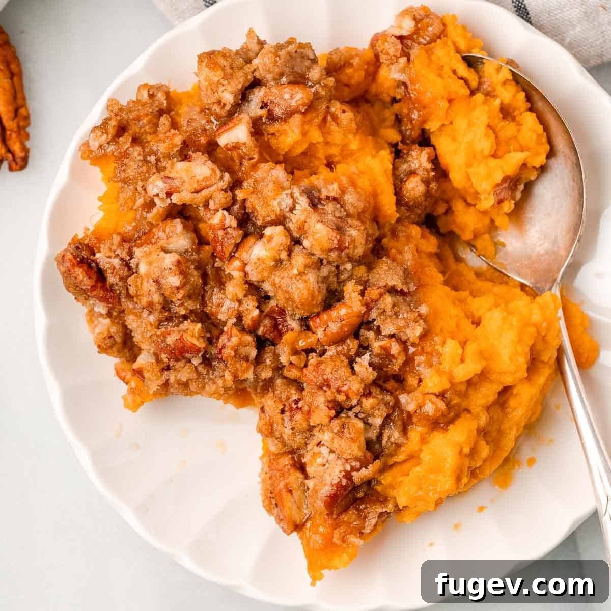 Golden Pecan Sweet Potato Bake 12 A serving of maple sweet potato casserole with a generous pecan topping on a white plate, ready to be enjoyed.