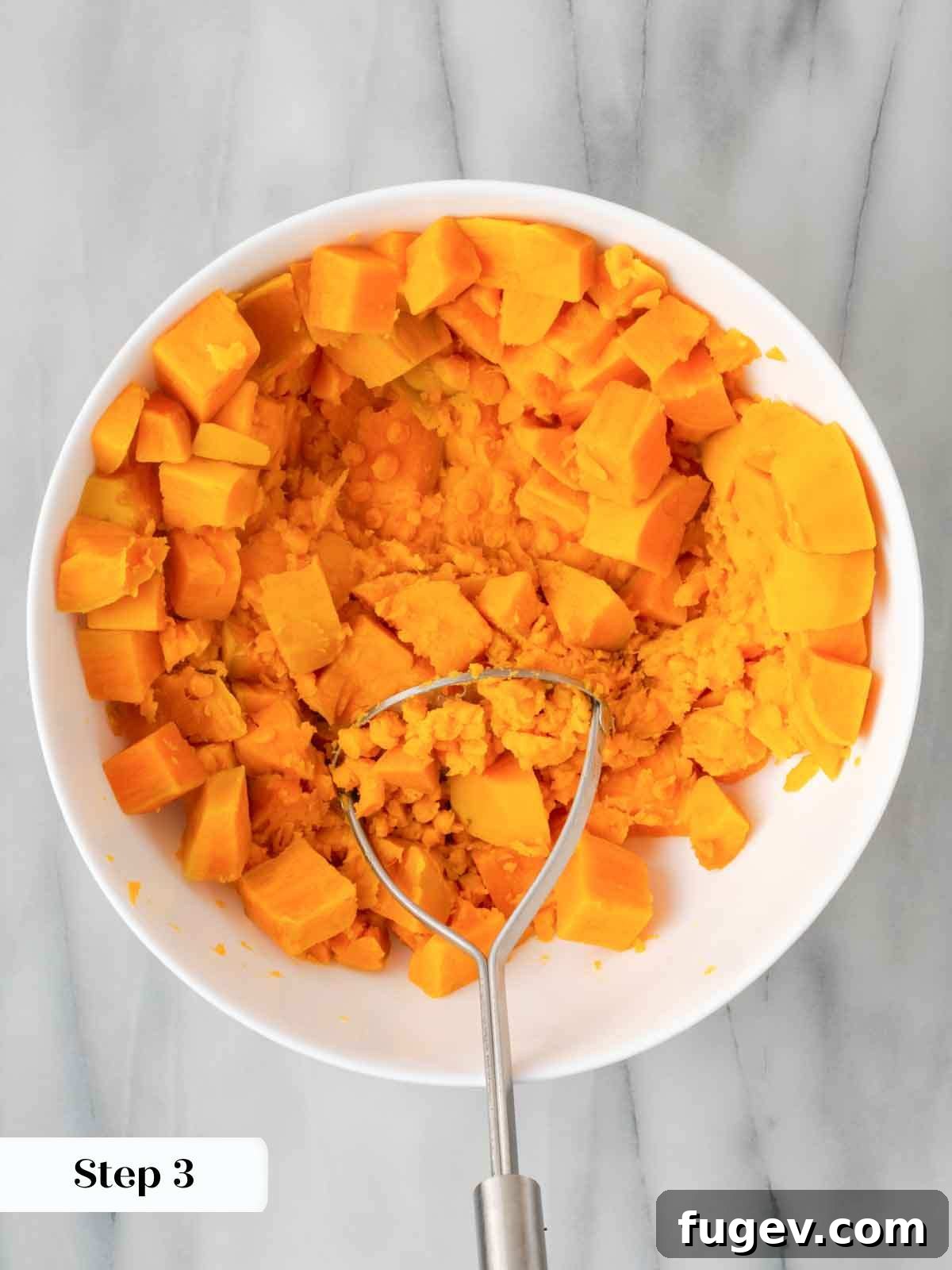 Golden Pecan Sweet Potato Bake 7 Mashing cooked sweet potatoes in a mixing bowl with a potato masher.
