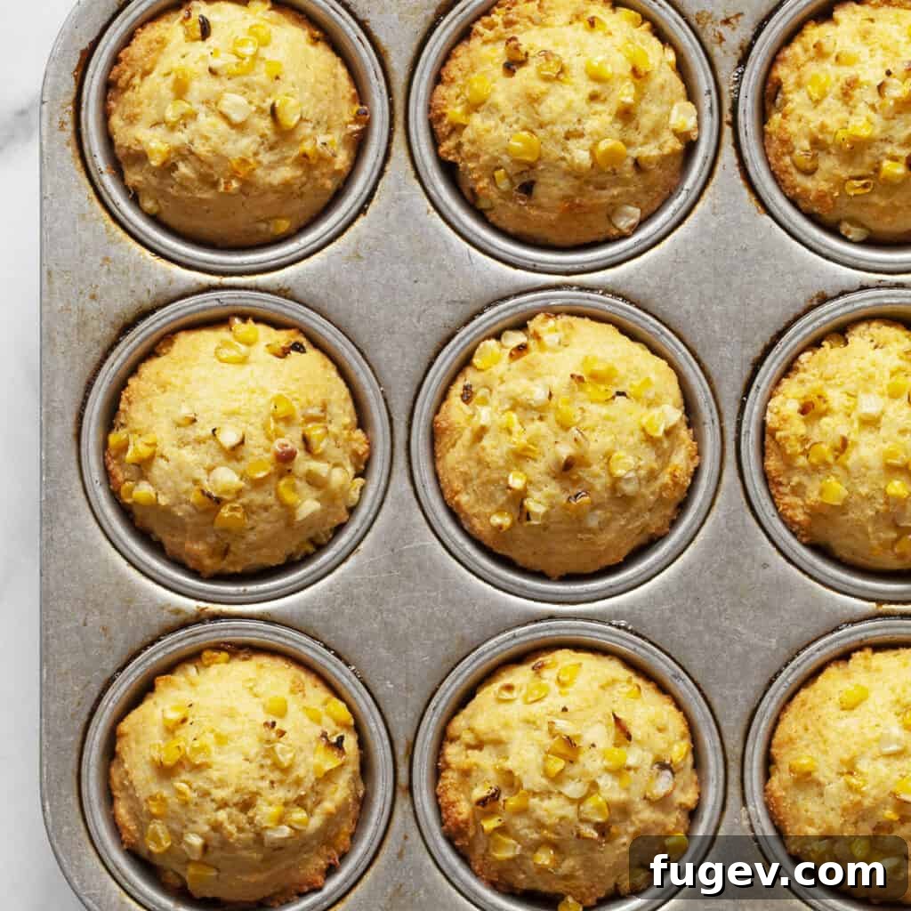 Smoky Sweet Cornbread Muffins 2 Golden cornbread muffins resting in a metal muffin pan, showcasing their perfectly baked tops and inviting texture.