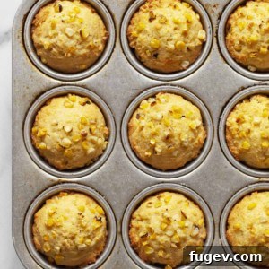 Cornbread muffins in a muffin pan, showcasing their golden tops.