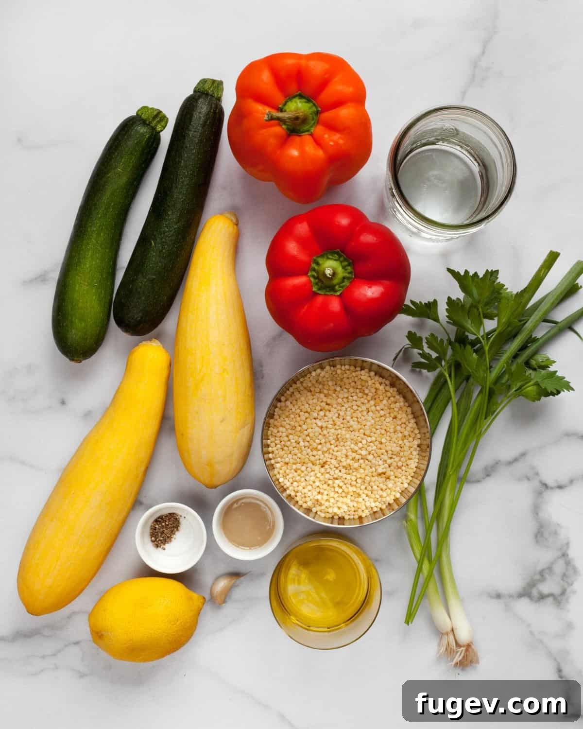 Bright Lemon Tahini Roasted Vegetable Couscous 3 A flat lay image displaying fresh ingredients for roasted vegetable couscous, including zucchini, bell peppers, yellow squash, scallions, parsley, lemon, and tahini, ready for preparation.