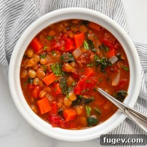 A bowl of hot green lentil soup, rich with vegetables and lentils, garnished with fresh herbs.