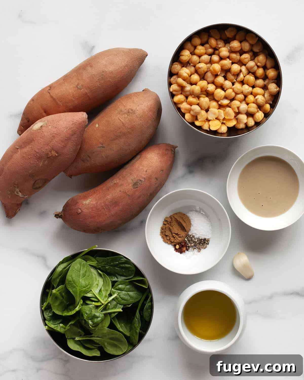 Savory Chickpea and Spinach Stuffed Sweet Potatoes 3 A selection of fresh ingredients including sweet potatoes, canned chickpeas, fresh spinach, tahini, garlic, olive oil, and various spices arranged on a cutting board.