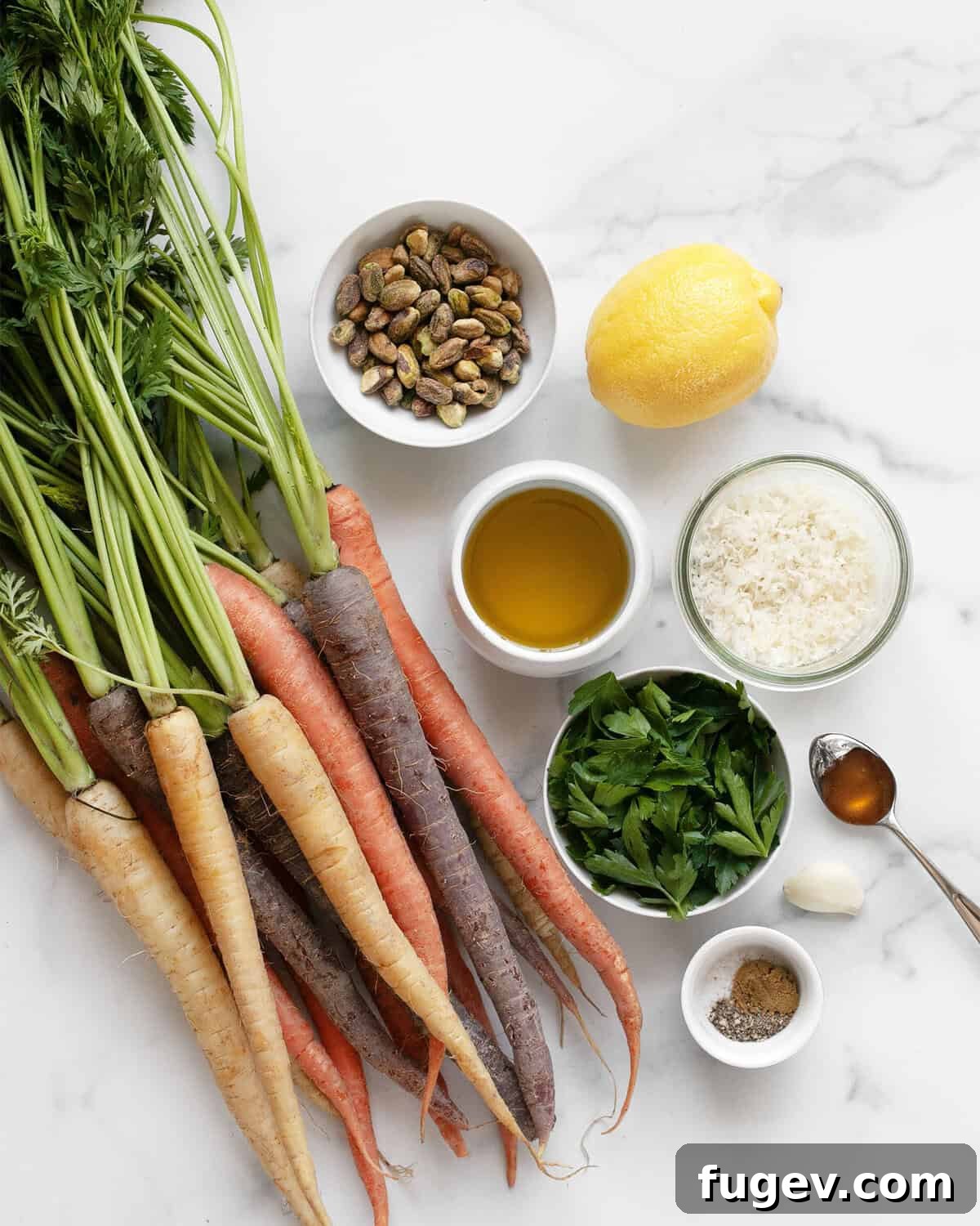 Roasted Rainbow Carrots and Their Green Crown Pesto 3 A flat lay photograph showcasing all the fresh ingredients needed for roasted rainbow carrots and carrot top pesto, including colorful carrots, pistachios, lemon, parsley, honey, cumin, salt, pepper, parmesan cheese, and olive oil.