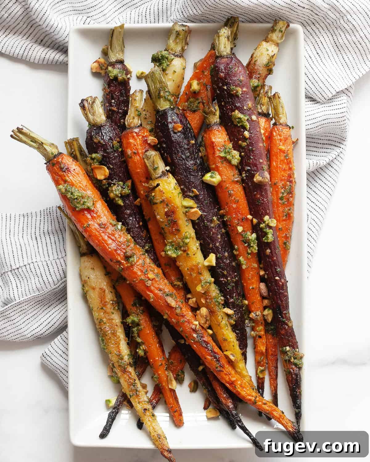 Roasted Rainbow Carrots and Their Green Crown Pesto 7 Roasted rainbow carrots with carrot top pesto beautifully arranged on a rectangular white serving plate, highlighting their vibrant colors and fresh appeal.