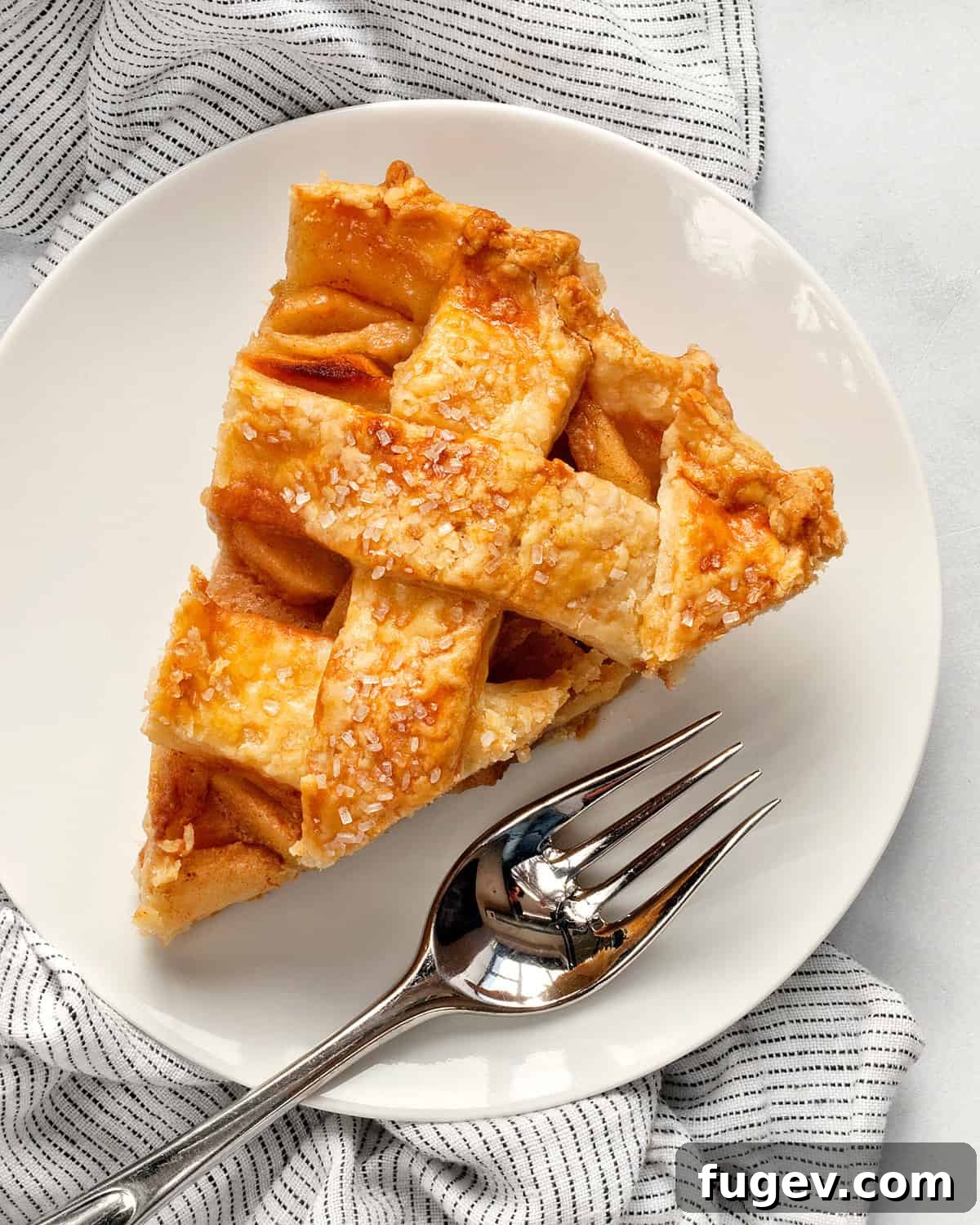 Salted Caramel Apple Crumble Pie 3 A delectable slice of lattice apple pie with a scoop of vanilla ice cream, served on a white plate.