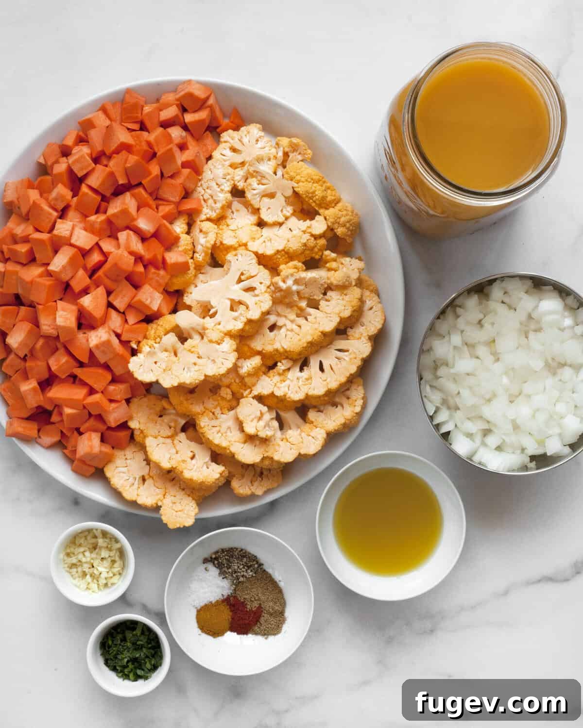 Golden Roasted Sweet Potato Cauliflower Soup 3 A vibrant display of fresh ingredients: sweet potatoes, cauliflower florets, vegetable broth, yellow onions, a bottle of olive oil, a variety of dried spices, cloves of garlic, and a bunch of fresh parsley.