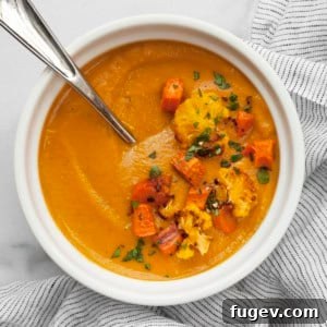 A heartwarming bowl of roasted sweet potato cauliflower soup, garnished with vibrant green parsley and reserved roasted vegetables.