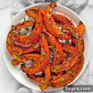 Roasted squash wedges on a plate, garnished with scallions and sesame seeds.