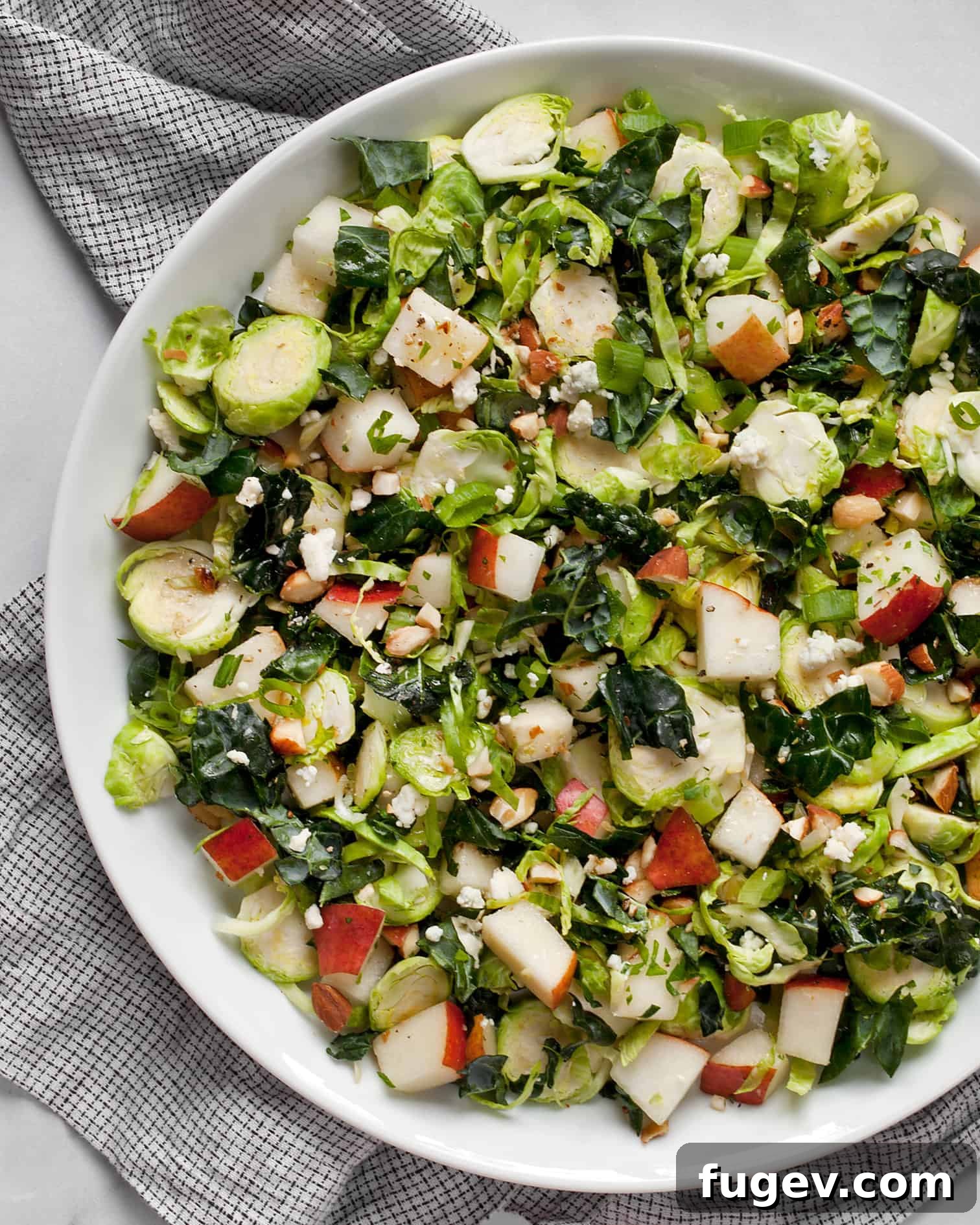Sweet Pear and Shaved Brussels Kale Salad 5 A close-up shot of the kale and brussels sprout salad with pears, blue cheese, and almonds in a white bowl, highlighting the fresh ingredients and inviting textures.