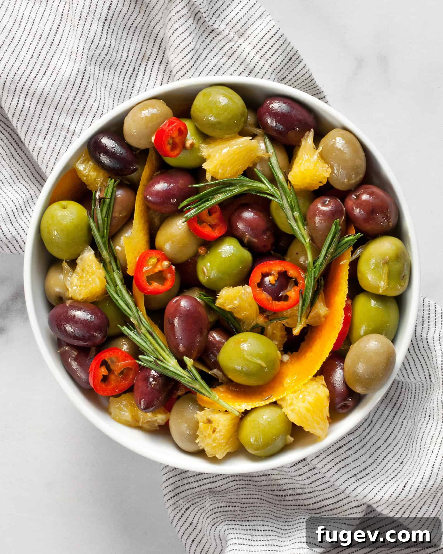 Zesty Herb Infused Olives 2 A bowl filled with beautifully marinated olives, vibrant orange segments, and fresh rosemary sprigs, ready to be served as an appetizer.
