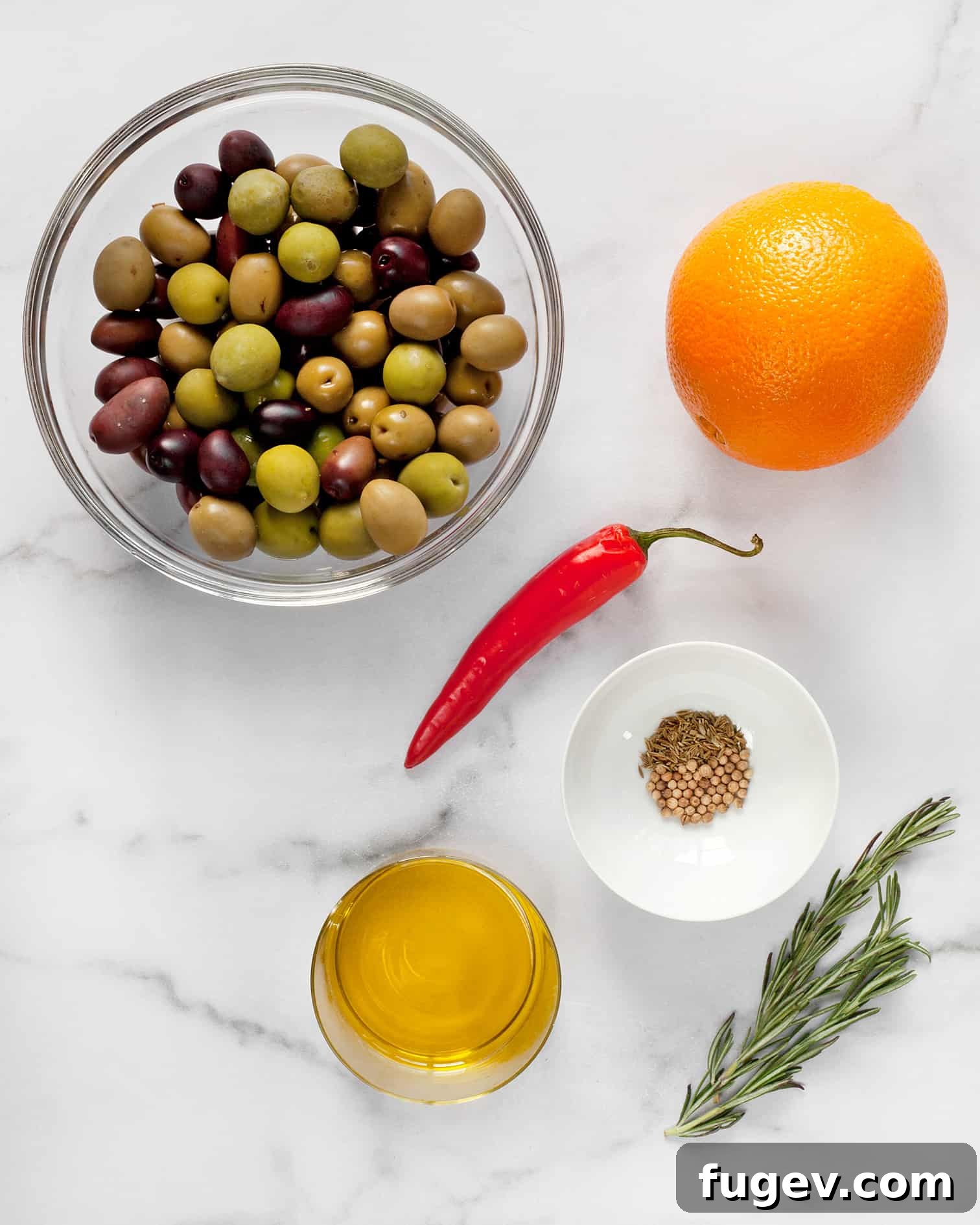 Zesty Herb Infused Olives 3 Individual ingredients laid out: mixed olives, a whole orange, fresh red chili, coriander and cumin seeds, rosemary sprigs, and a bottle of olive oil, ready for preparation.