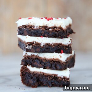 Close-up of three peppermint triple chocolate brownies, showing the thick frosting and sprinkles, stacked on a cooling rack.