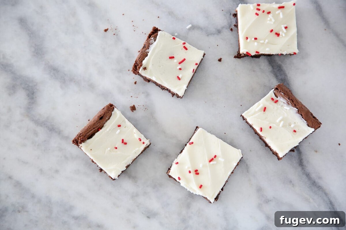Peppermint Fudge Brownies 6 Close-up of scattered peppermint brownies on a countertop, showing a rich, fudgy texture with creamy white frosting and visible peppermint pieces.