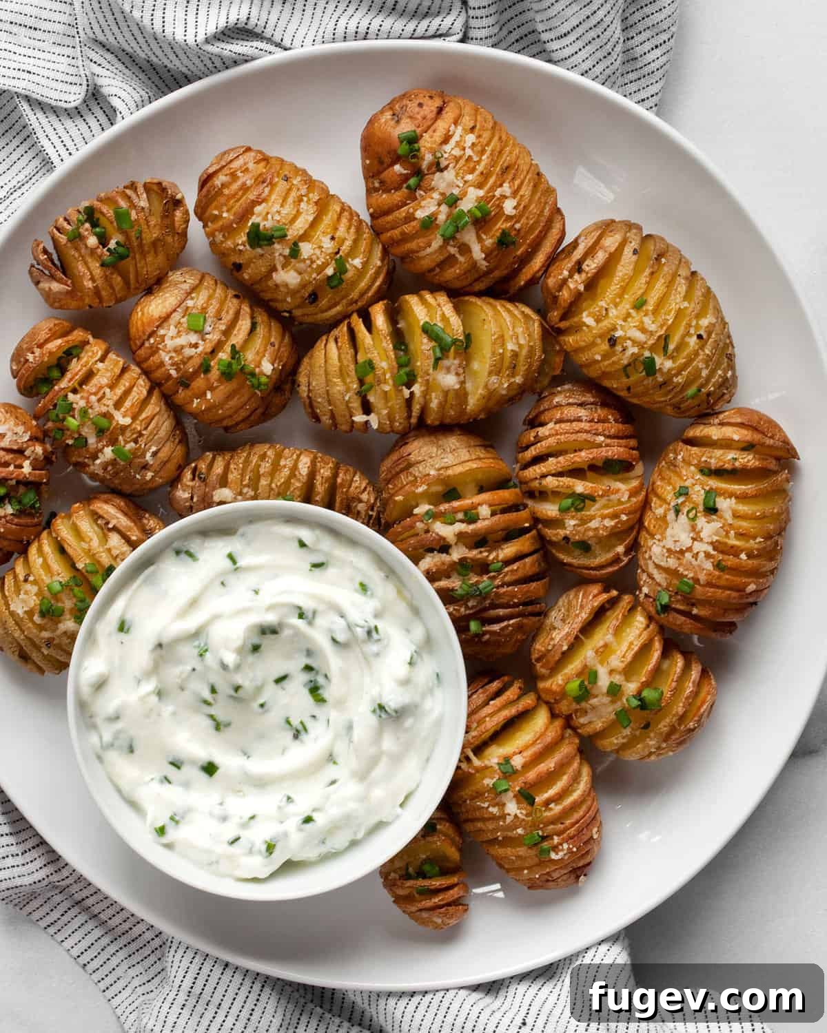 Crispy Accordion Bites 8 A delightful close-up of mini hasselback potatoes arranged on a plate, with a small bowl of vibrant green herby yogurt dip to the side.