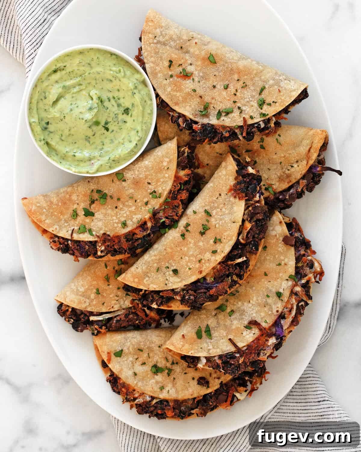 Crispy black beans tacos arranged beautifully on a serving plate, accompanied by a small bowl of creamy avocado sauce.