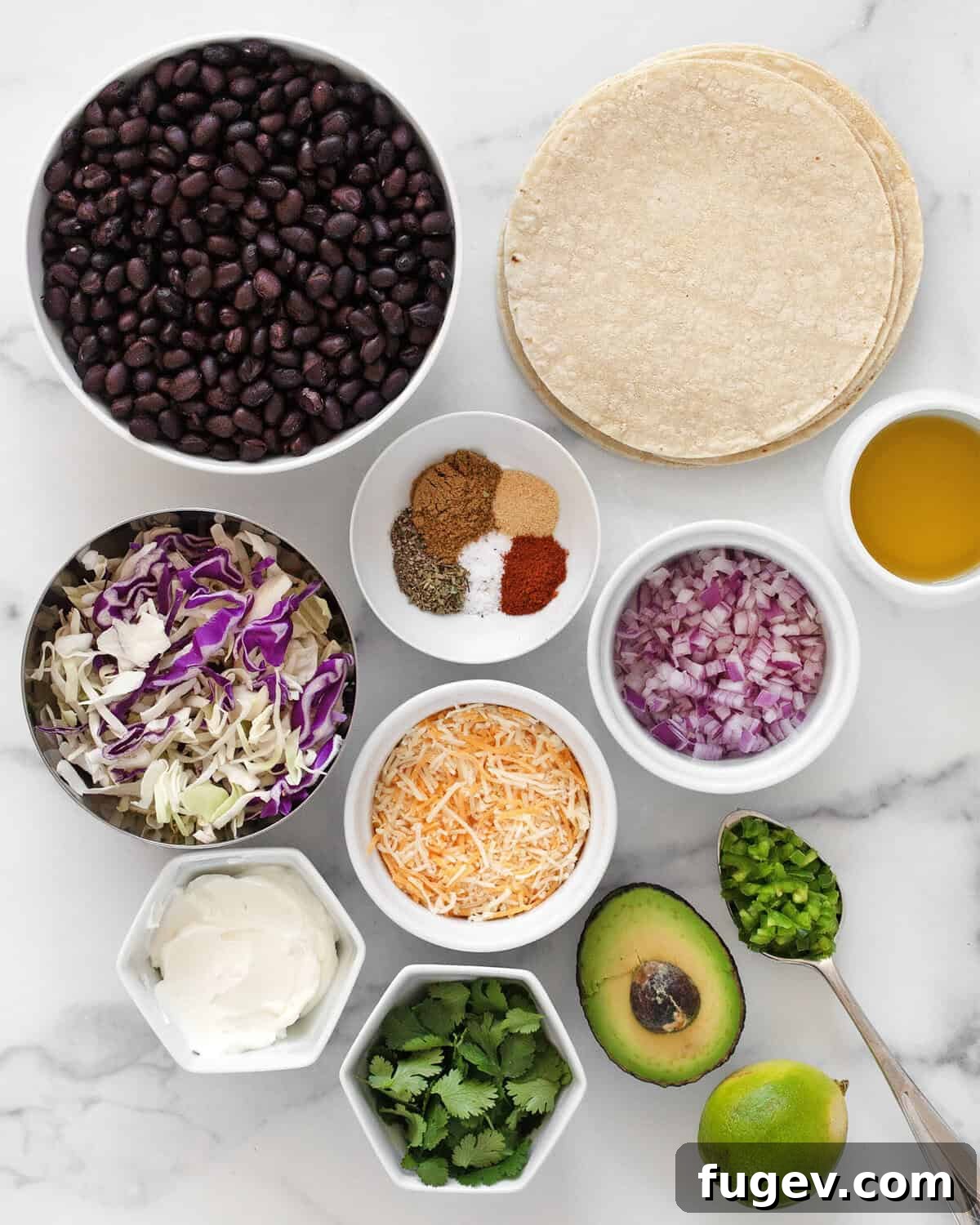 A vibrant flat lay of all ingredients for crispy black bean tacos including corn tortillas, black beans, red onions, cabbage, various spices, shredded cheese, avocado, jalapenos, Greek yogurt, cilantro, lime, and olive oil.
