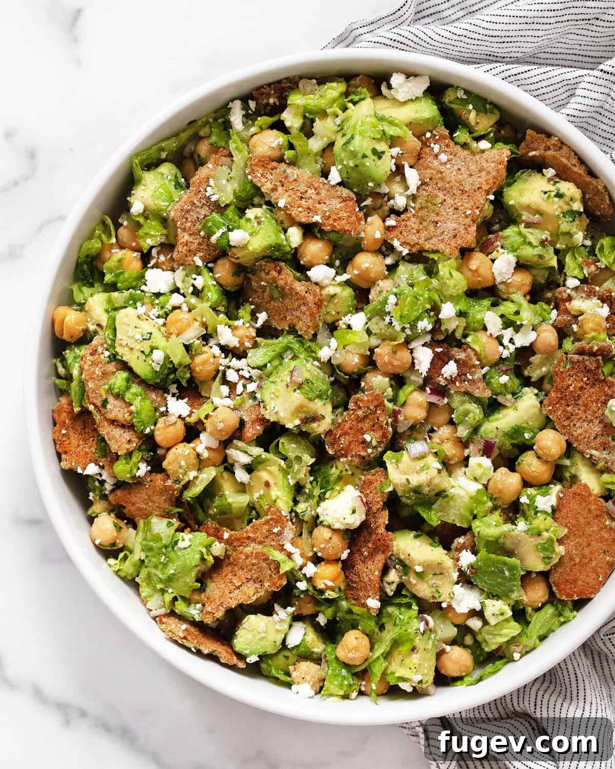 Freshly prepared chickpea avocado salad in a rustic serving bowl, generously garnished with fresh herbs and crispy pita chips.