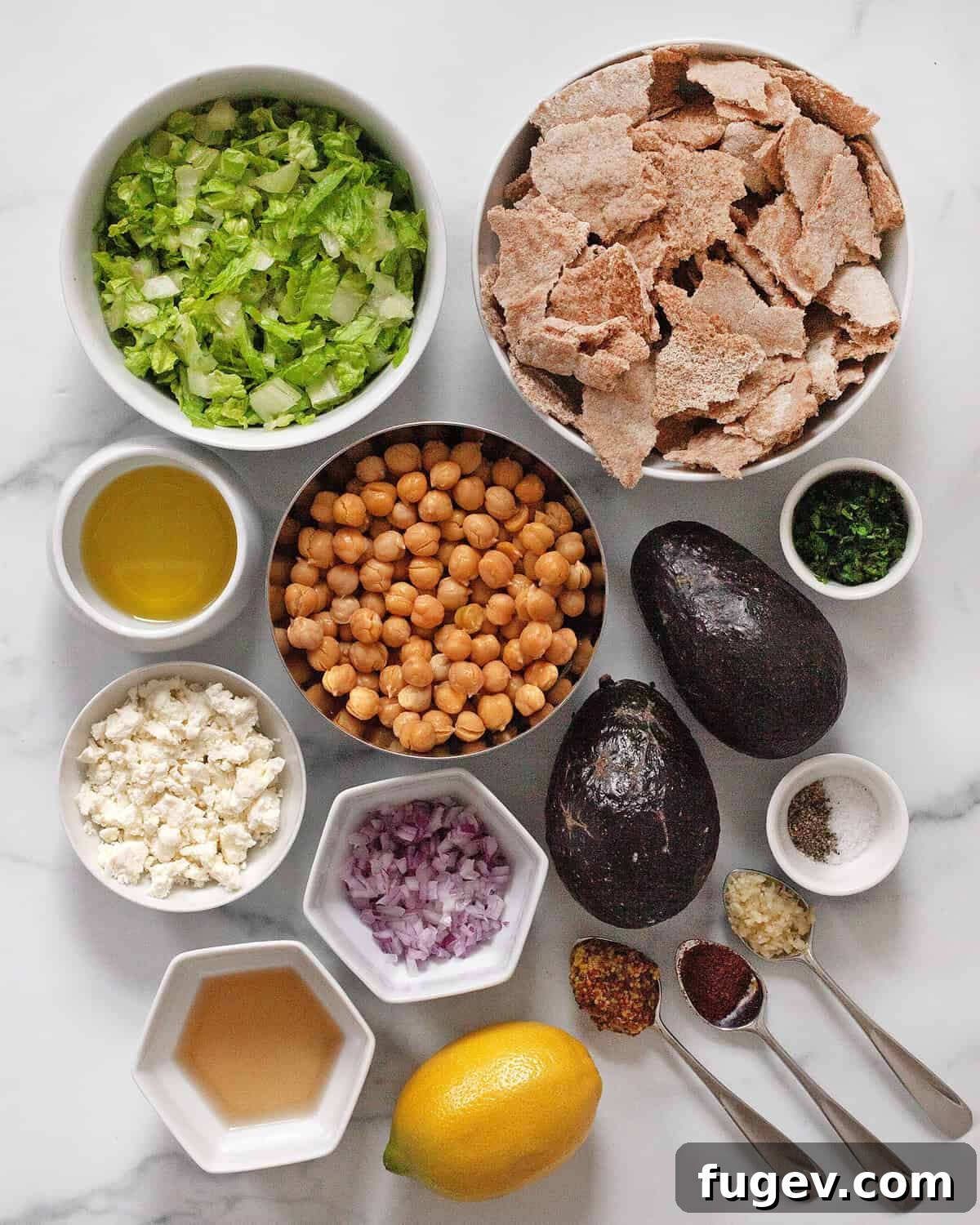 An array of fresh ingredients neatly arranged for chickpea avocado salad: canned chickpeas, ripe avocados, whole wheat pita bread, crumbled feta cheese, crisp shredded romaine, thinly sliced red onions, fresh lemon, olive oil, garlic, whole grain mustard, sumac, and basic salt and pepper.