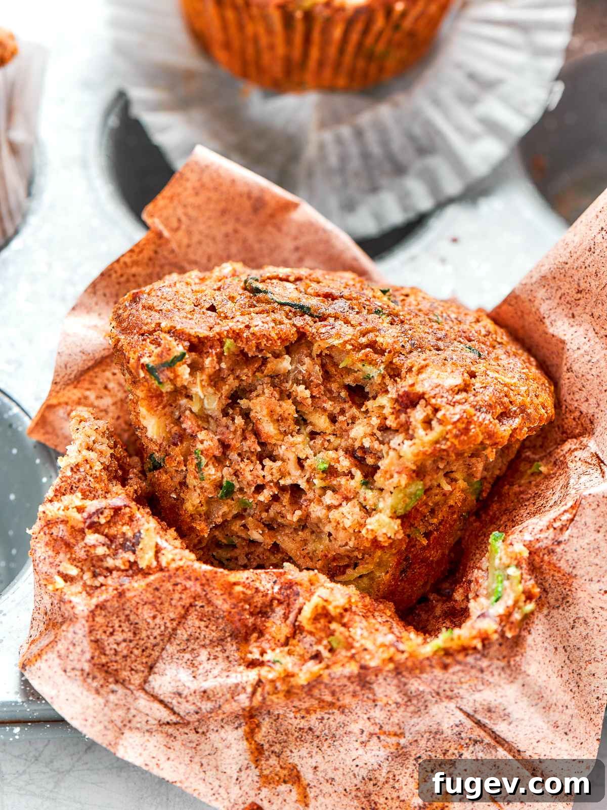 Zucchini muffin split open revealing soft tender crumb and flecks of zucchini, highlighting its moist texture and healthy ingredients.