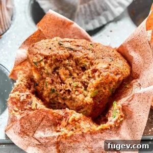 Zucchini muffin with a bite taken, showcasing its moist crumb and visible flecks of fresh green zucchini, ready to be eaten.