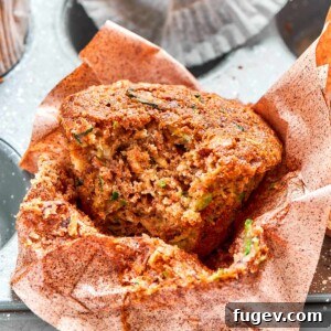 A freshly baked zucchini muffin with a bite taken, showing its moist crumb and vibrant green flecks of zucchini.