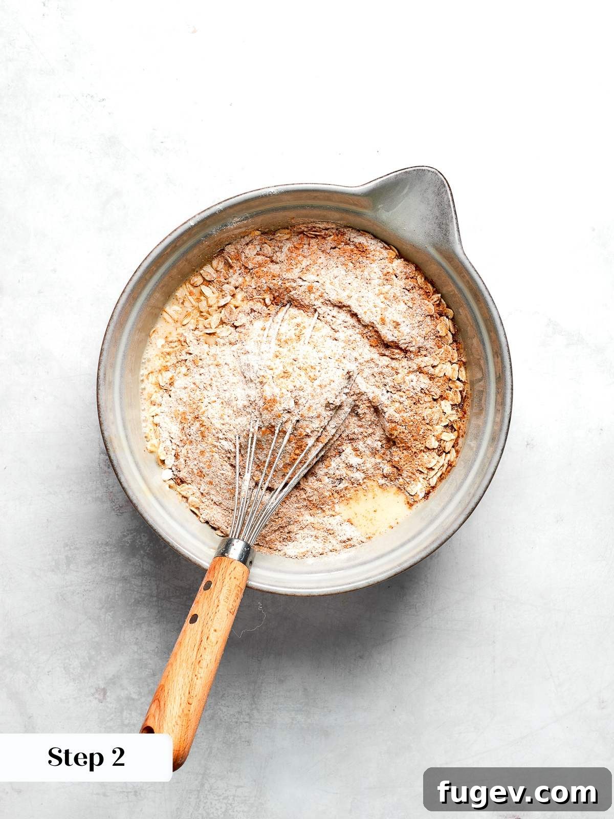 Dry ingredients including whole wheat flour, oats, flax, and various spices are whisked together in a medium bowl, ready for the muffin batter.