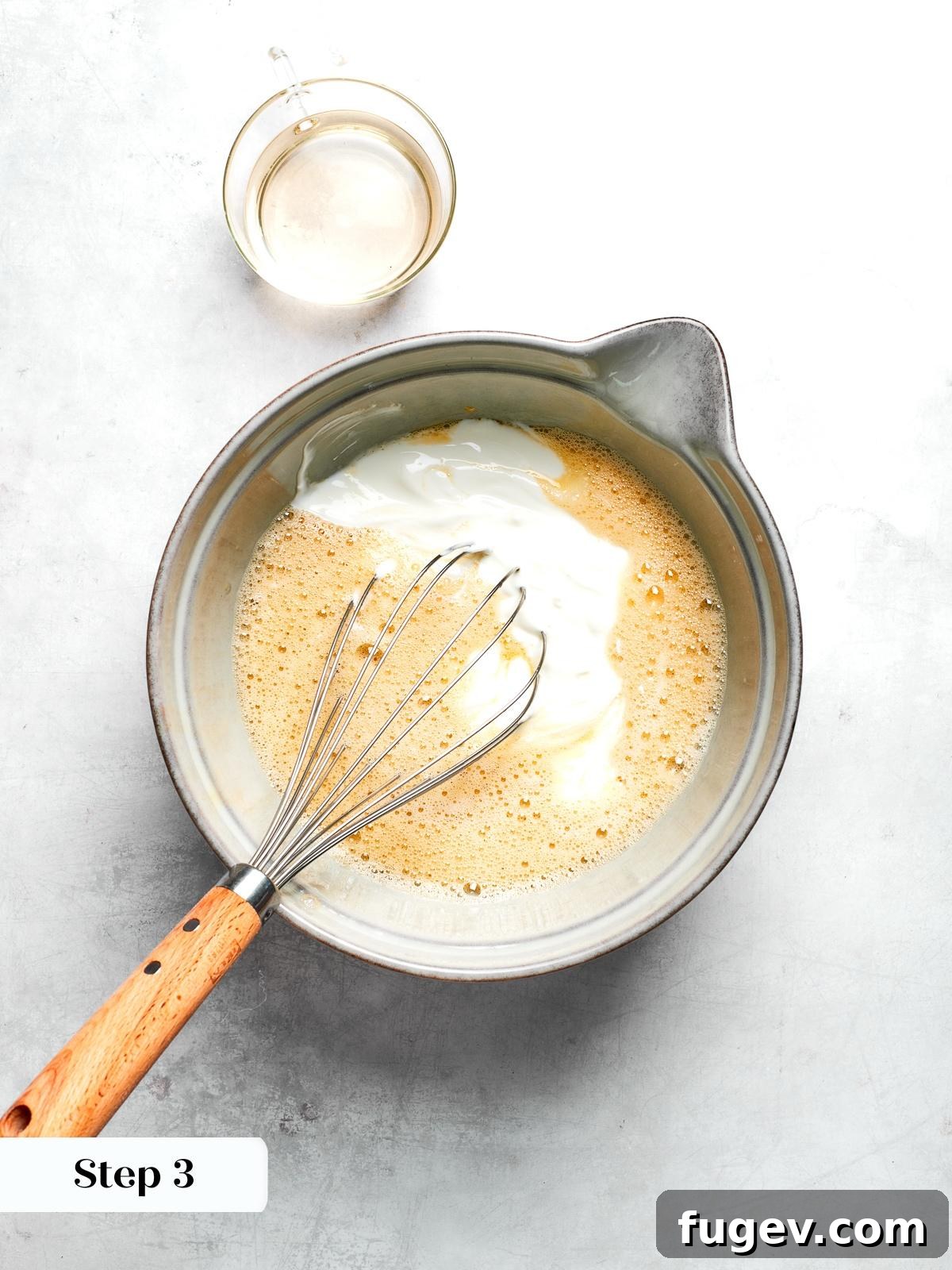 Wet ingredients such as Greek yogurt, maple syrup, and egg being whisked vigorously together in a large mixing bowl for the zucchini muffin batter.