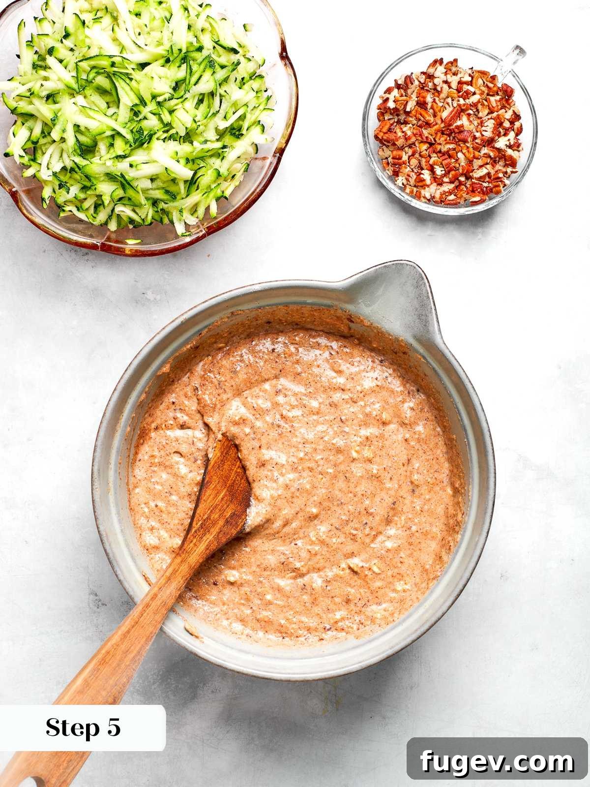 The process of gently mixing wet and dry ingredients together to form a cohesive zucchini muffin batter, ensuring not to overmix.