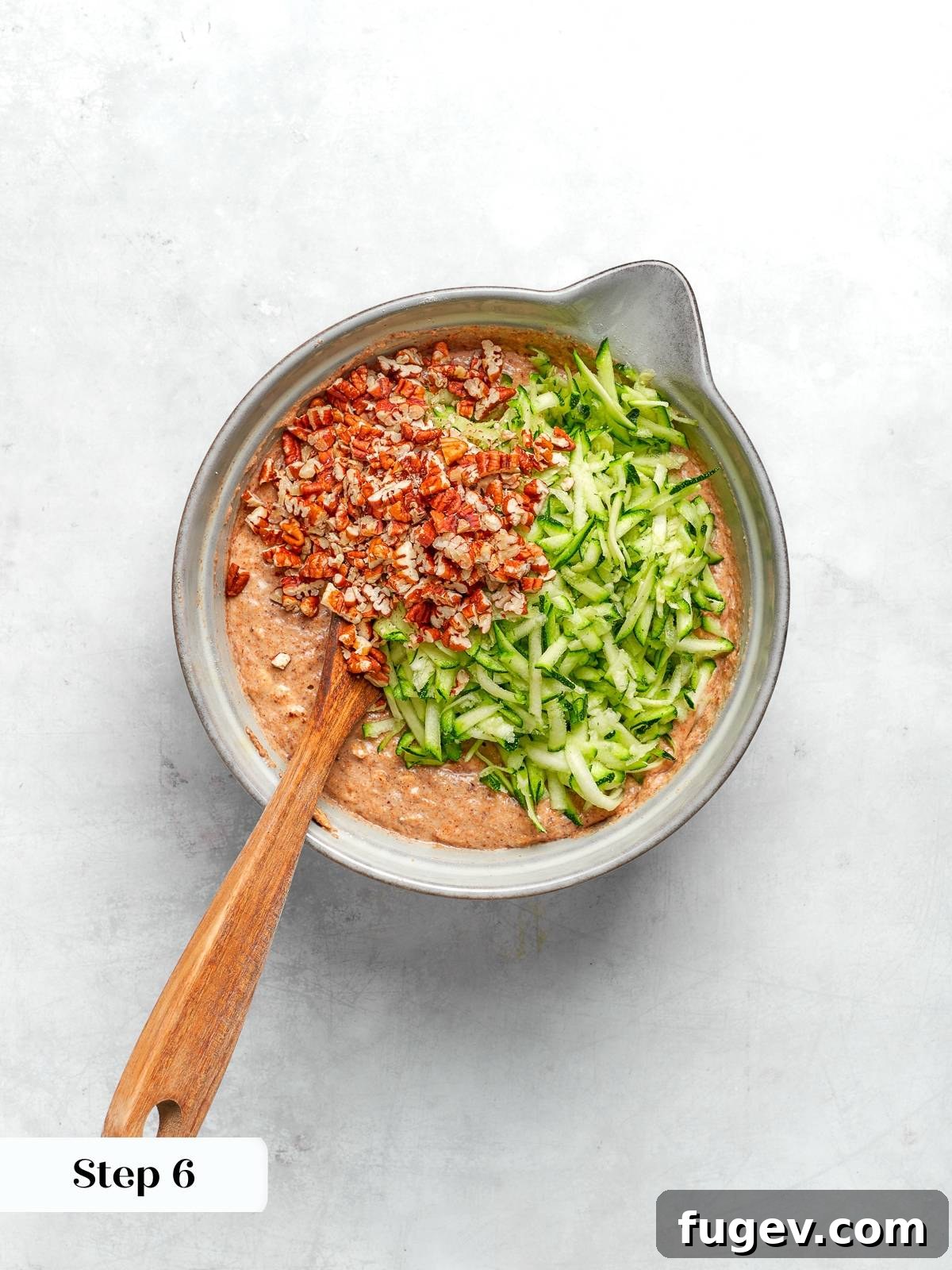 Finely shredded zucchini and chopped toasted pecans being carefully folded into the muffin batter, distributing them evenly without overmixing.