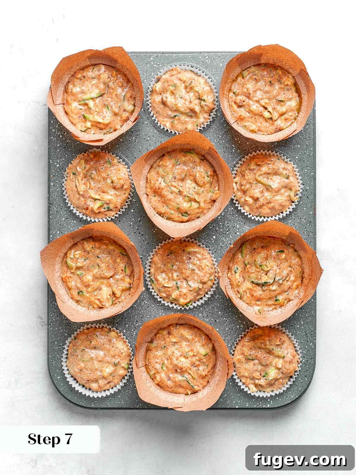 Zucchini muffin batter perfectly scooped into lined muffin cups, ready to be placed in the oven for baking.