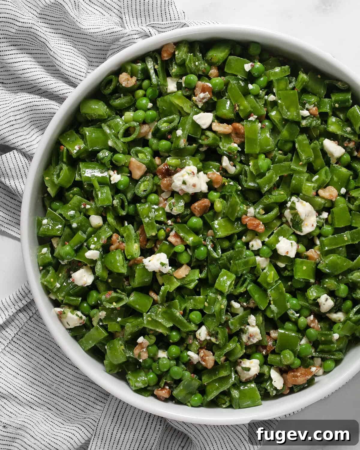 Triple Pea Delight 2 Three pea salad in a large serving bowl, showcasing vibrant green peas, crumbled feta, and toasted walnuts, ready to be served.