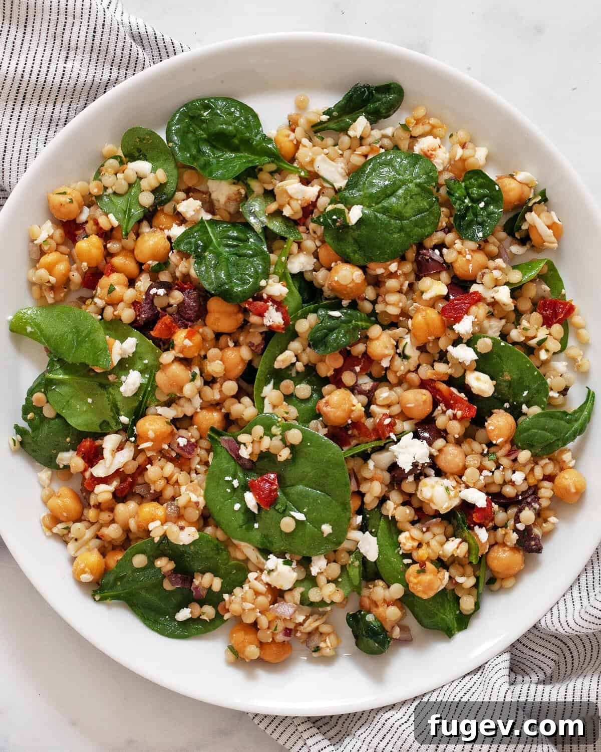 A beautifully arranged Mediterranean couscous salad on a white plate, showcasing its vibrant ingredients.