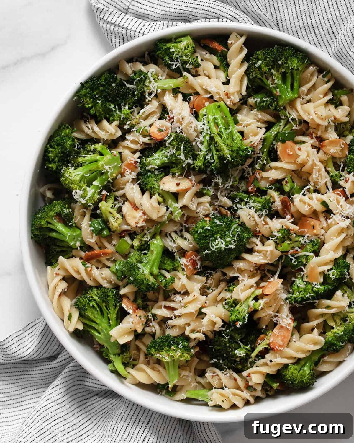 A vibrant bowl of roasted broccoli pasta salad, garnished with fresh herbs and almonds.