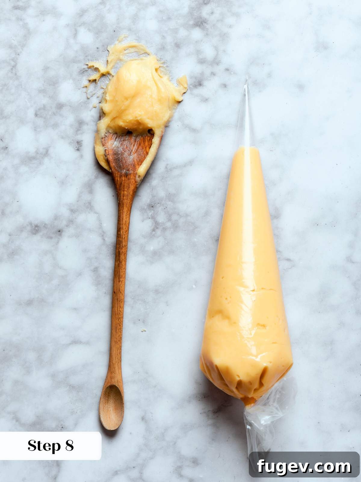 Smooth choux paste ready in a piping bag and scooped onto a spoon, against a marble background, highlighting its ideal consistency.