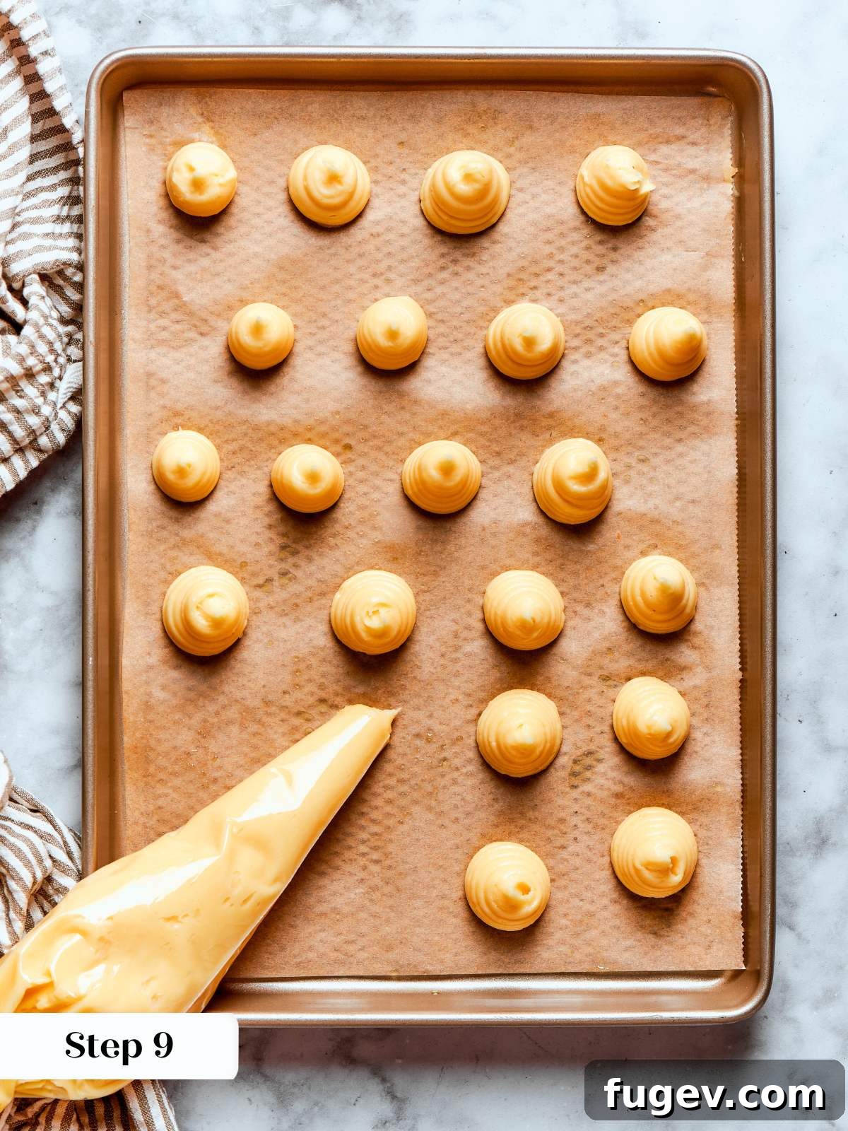 Precisely piped choux pastry rounds arranged neatly on brown parchment paper on a baking sheet, ready for the oven.
