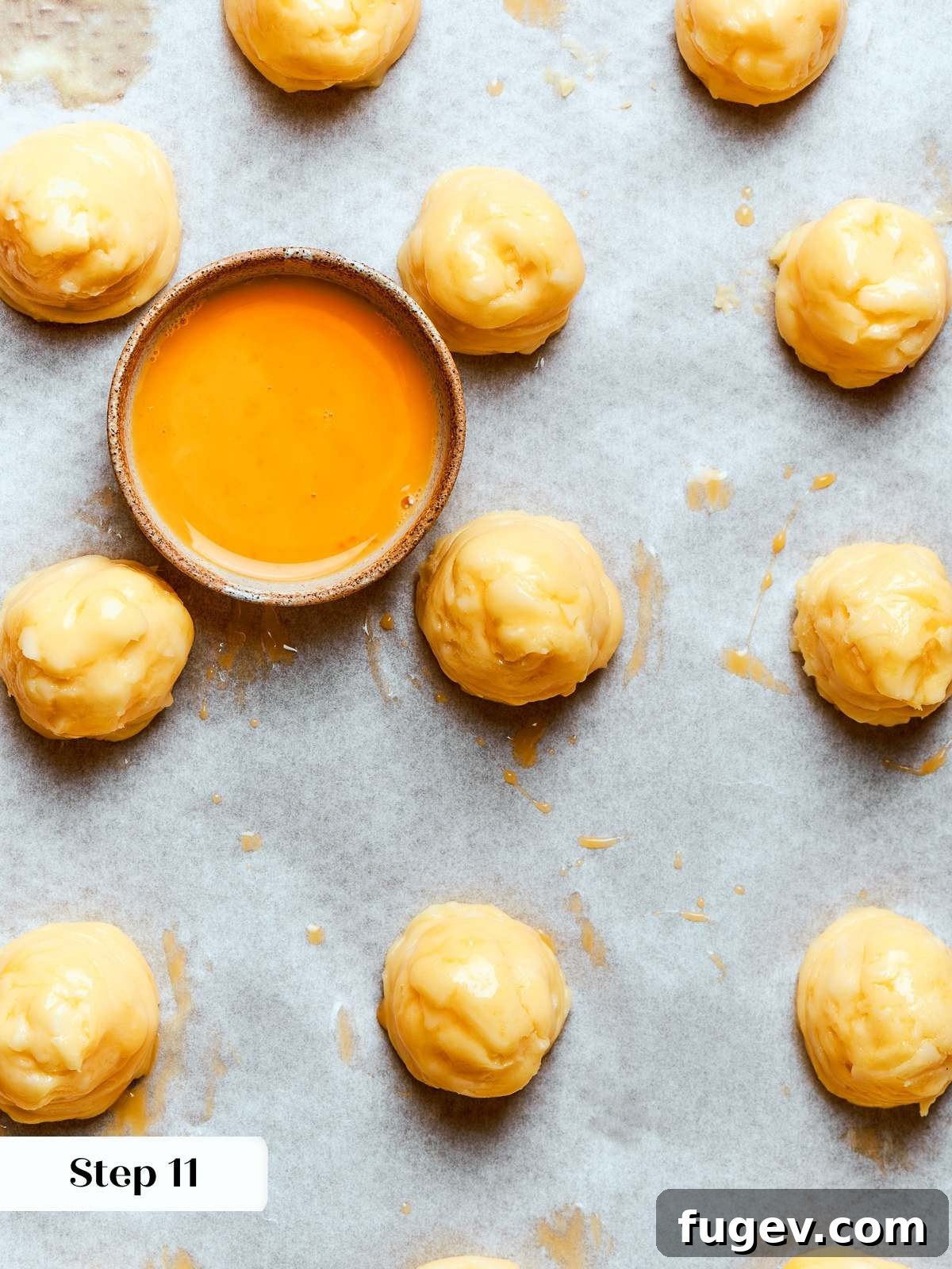 Golden Savory Puffs 19 Egg wash brushed over piped gougères smoothing tops and preparing for baking. The final touch before baking the cheese puffs.