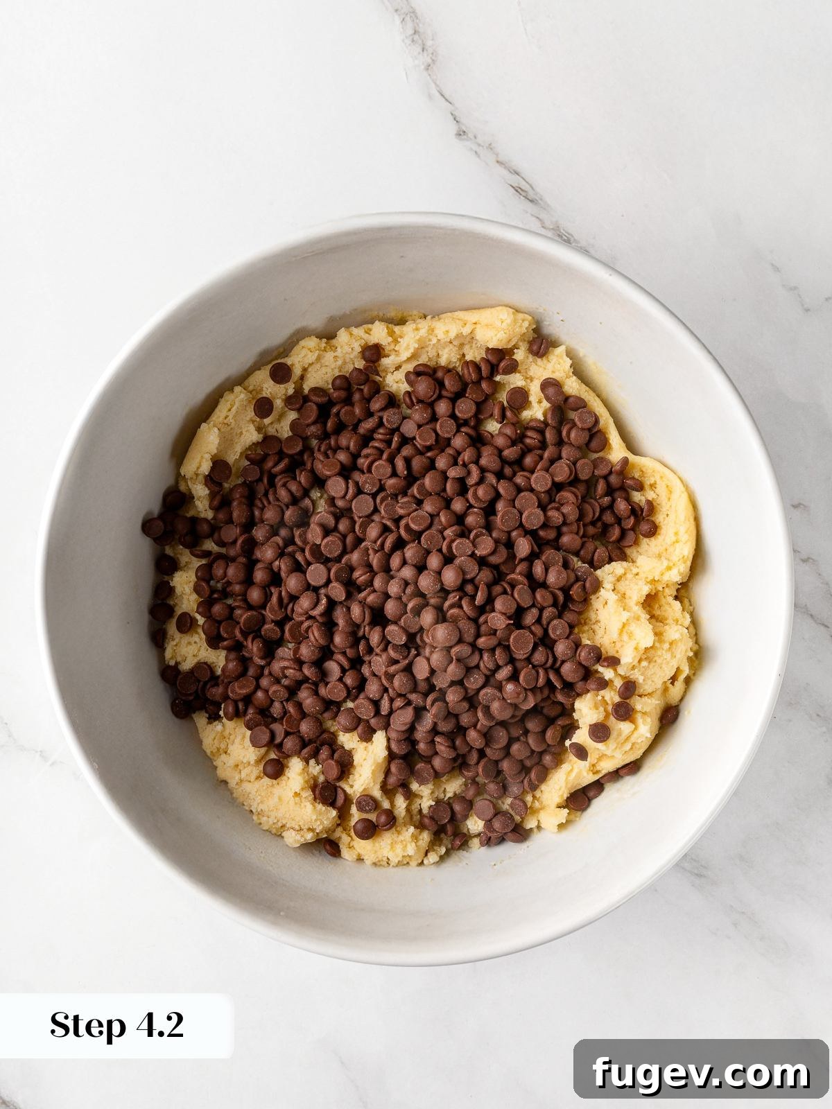 Semi-sweet chocolate chips being added to the finished cookie dough in the mixing bowl.