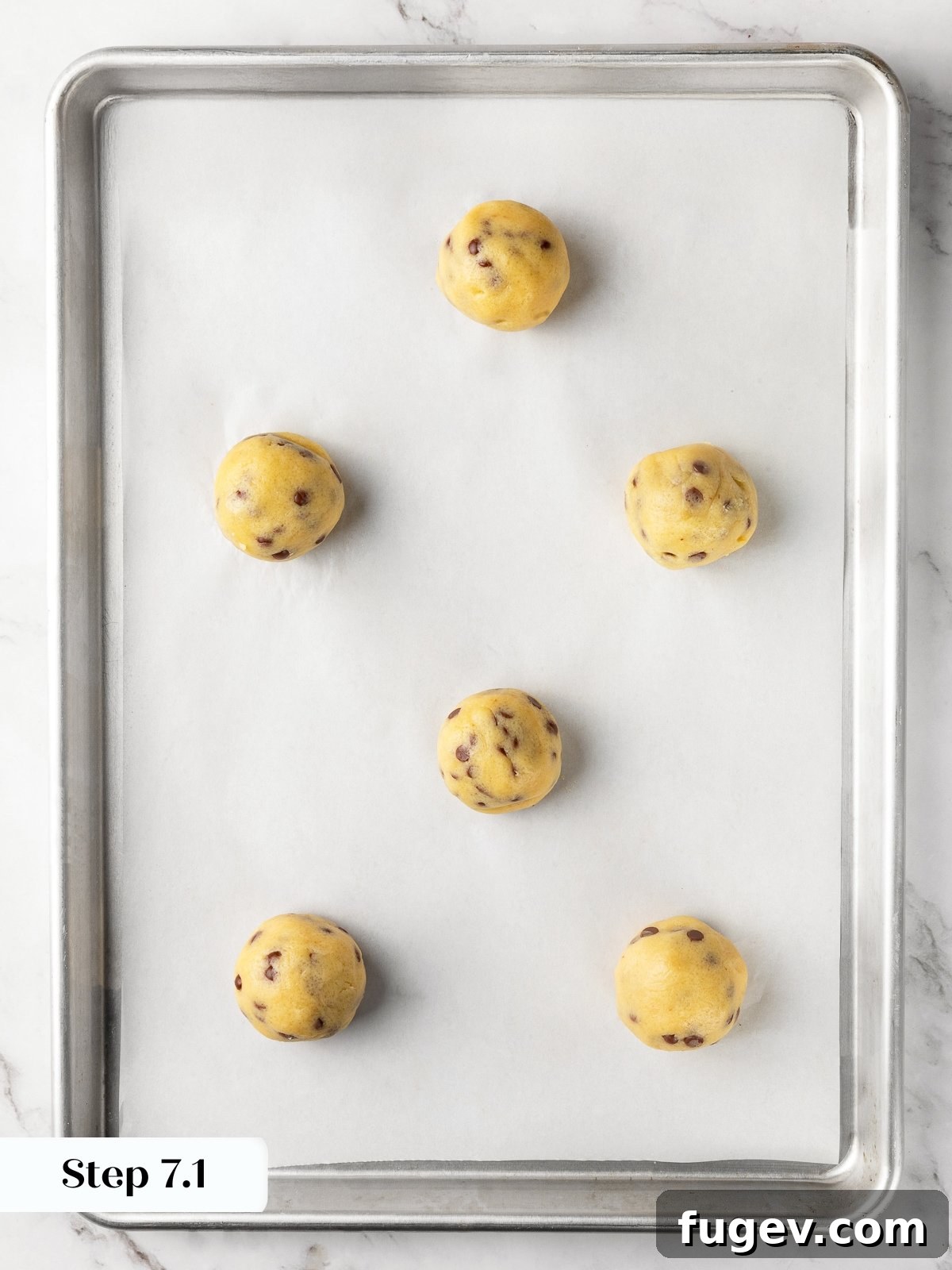 Chilled cookie dough balls spaced out on a parchment-lined baking sheet, ready to go into the oven.