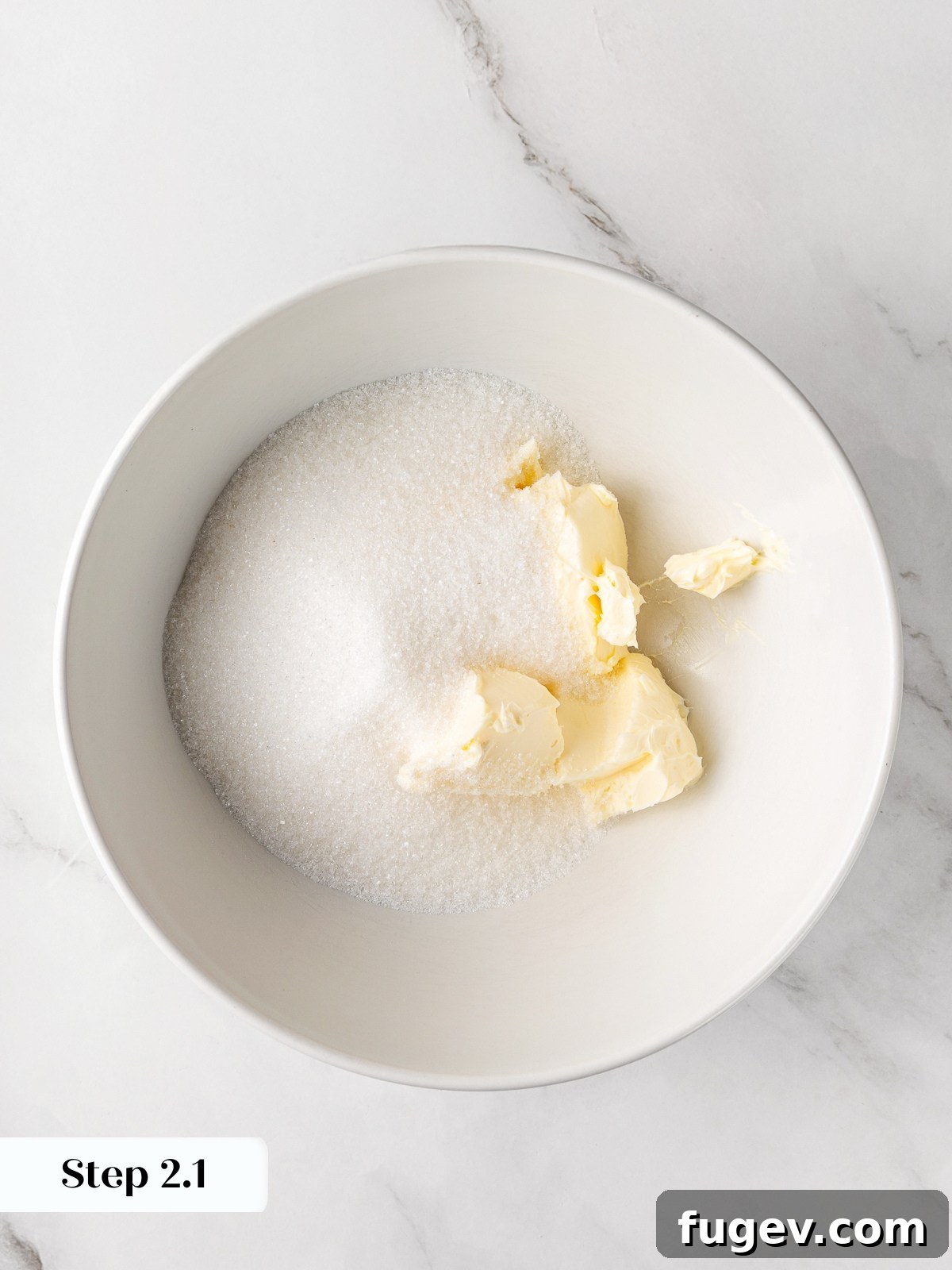 Softened butter and granulated sugar in a mixing bowl before being creamed together.