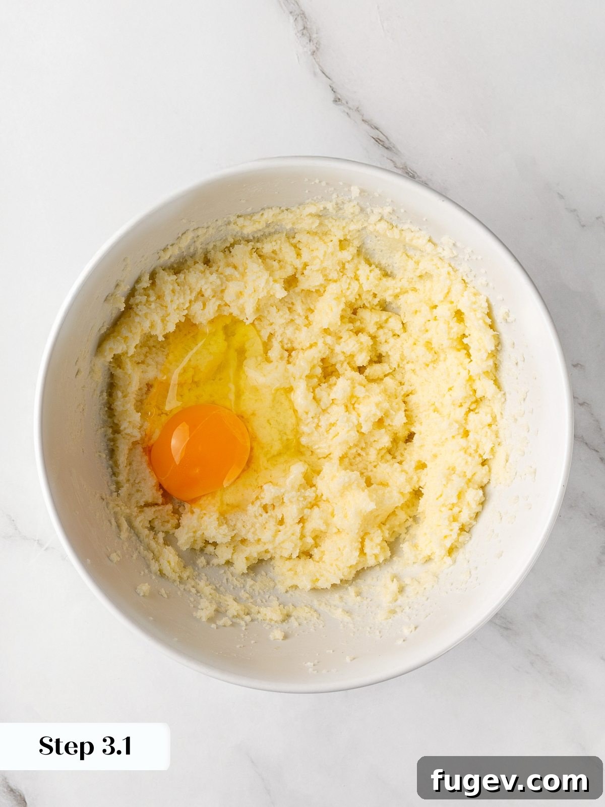 An egg being added to the creamed butter and sugar mixture in the stand mixer bowl.