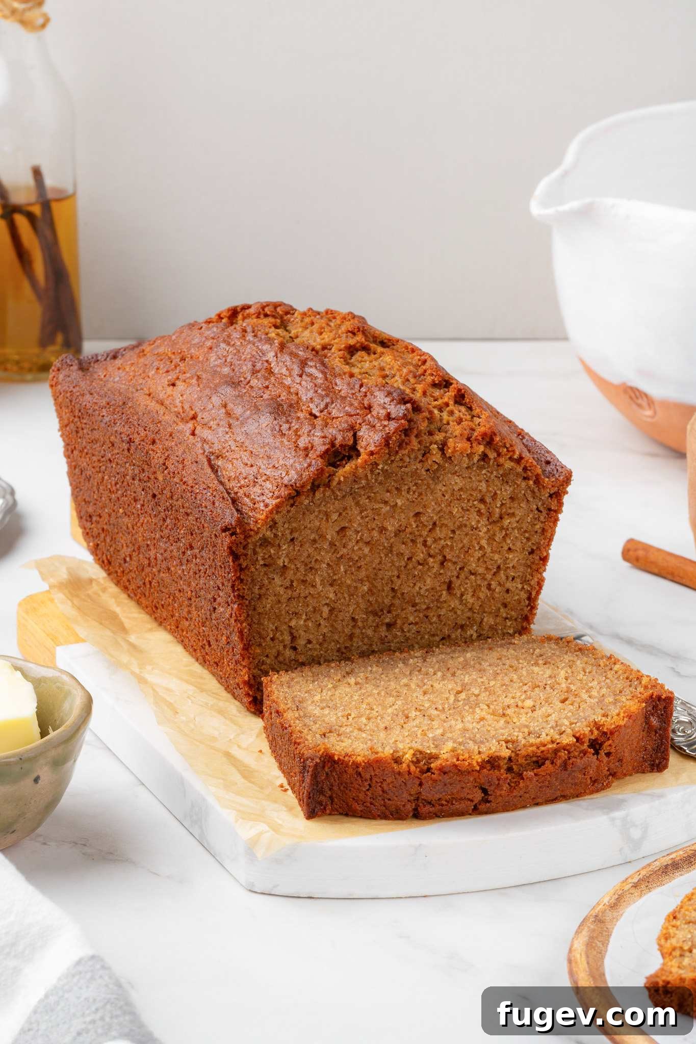 Tall caramelized loaf with a single freshly cut slice resting on parchment-lined wood and marble.