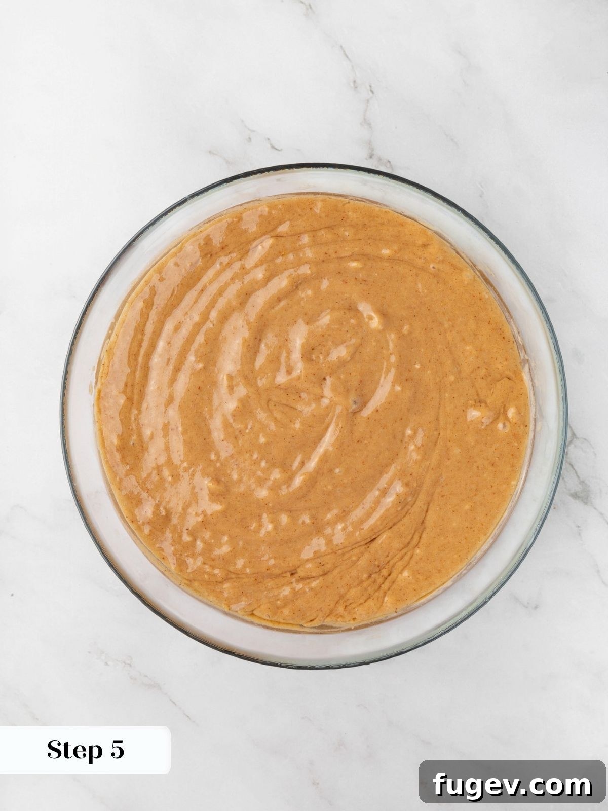 Smooth glossy batter swirled into a uniform pale orange after the warm coconut oil is added.