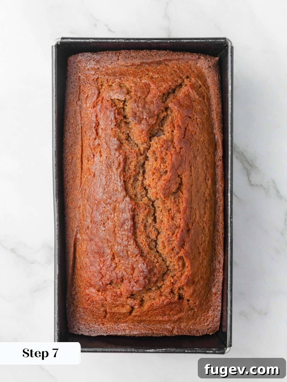 Deeply golden baked loaf with a cracked center crust still resting in its metal loaf pan.