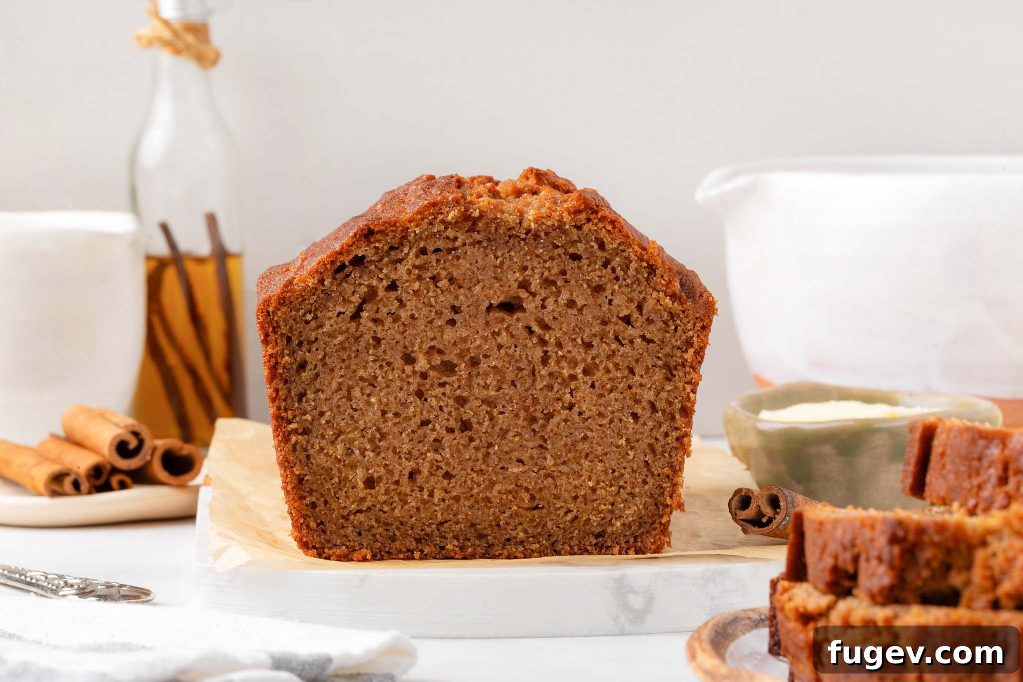 Cross-section of the loaf showing fine moist crumb framed by cinnamon sticks and a white pitcher.